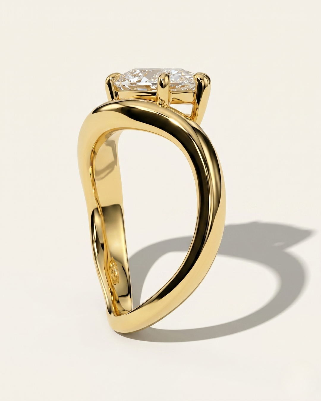 Side profile view of the MOHSTEN Venice pear diamond solitaire engagement ring in 18ct yellow gold, showcasing the unique low-profile setting and fluid, sweeping band architecture casting a distinct shadow on a light studio background.
