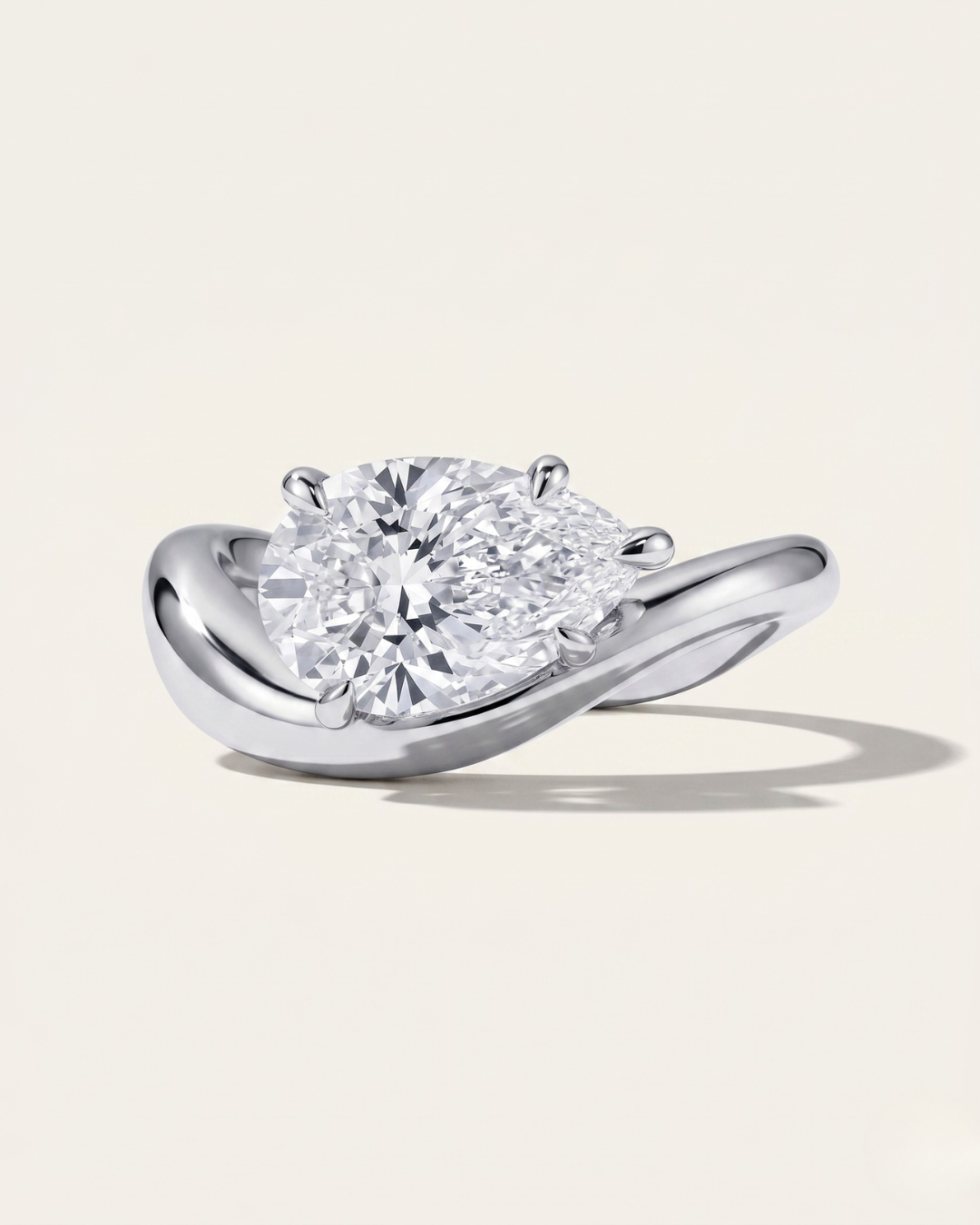 MOHSTEN Venice pear diamond solitaire engagement ring in polished platinum showcasing a face-on studio view of the east-west oriented pear-cut diamond on a fluid, sweeping curved band casting a distinct architectural shadow.