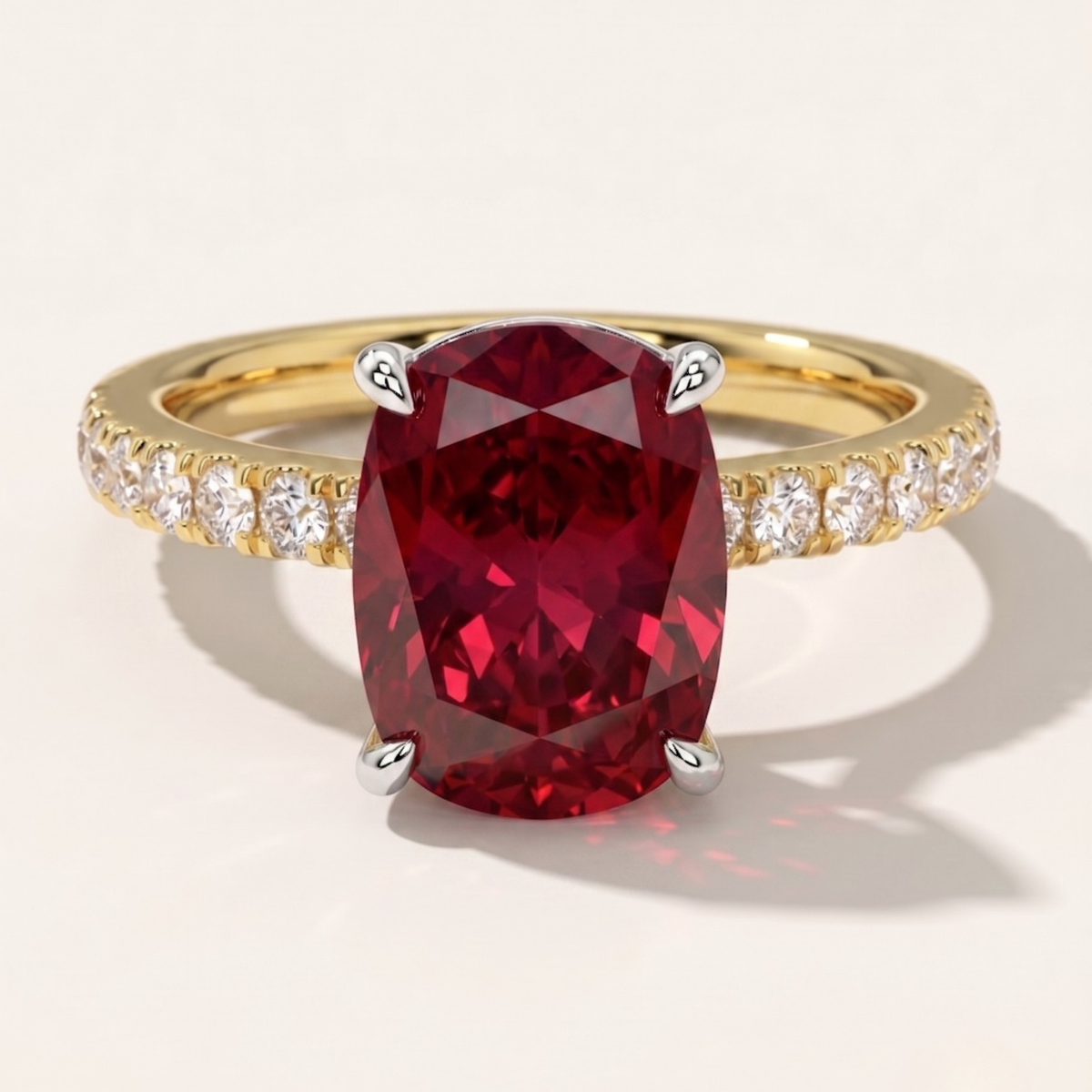 A MOHSTEN gold ring featuring a large oval-cut deep red ruby center stone in a four-prong setting, with a pavé band set with small clear round diamonds, shown on a light beige background.