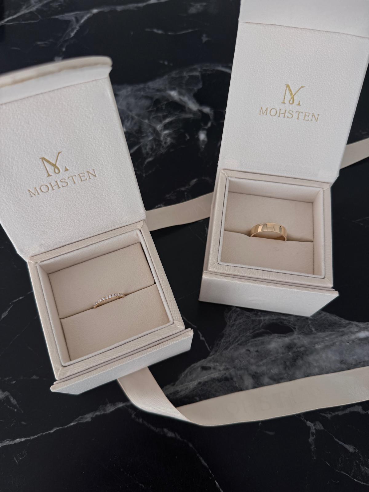 Jewelry box with gold ring inside on a dark marble surface, featuring the brand 'MOHSTEN'.