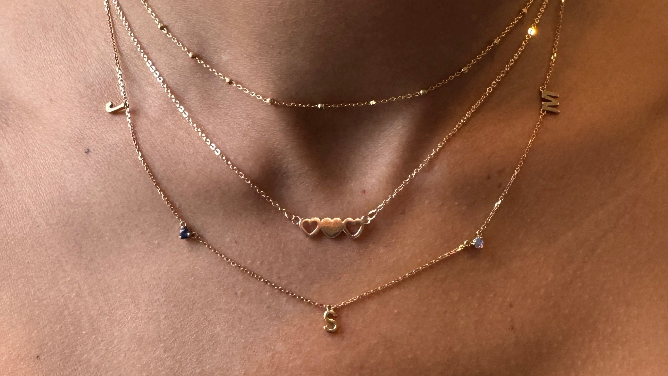 Close-up of a person wearing multiple gold necklaces with small pendants on a neutral background