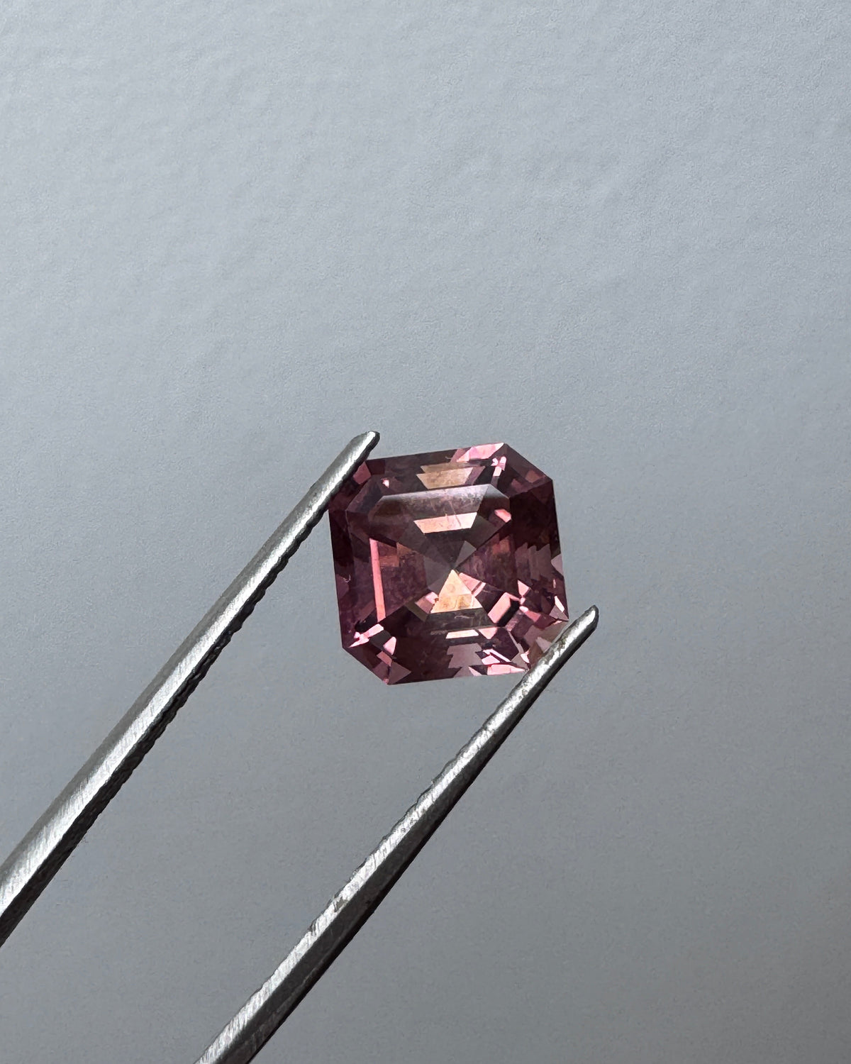 A faceted pink tourmaline held between metal tweezers.