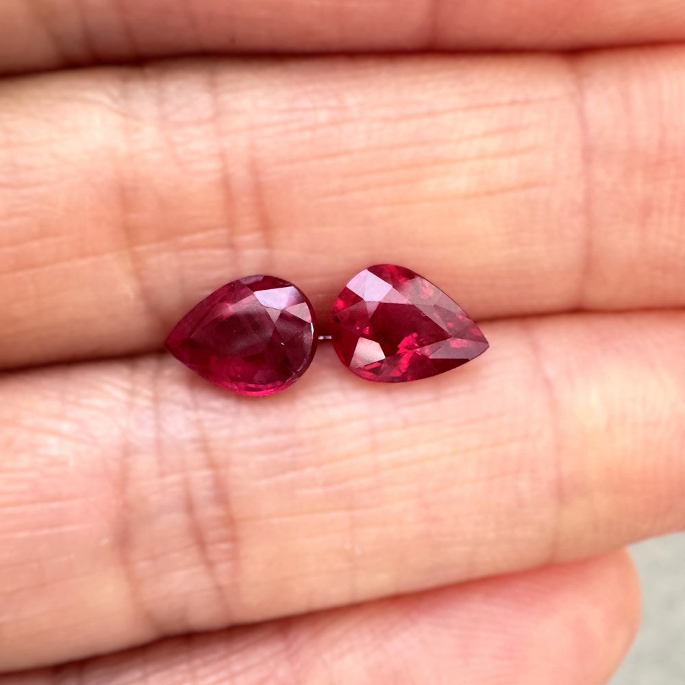 Two red ruby pear cut loose held between fingersbackground