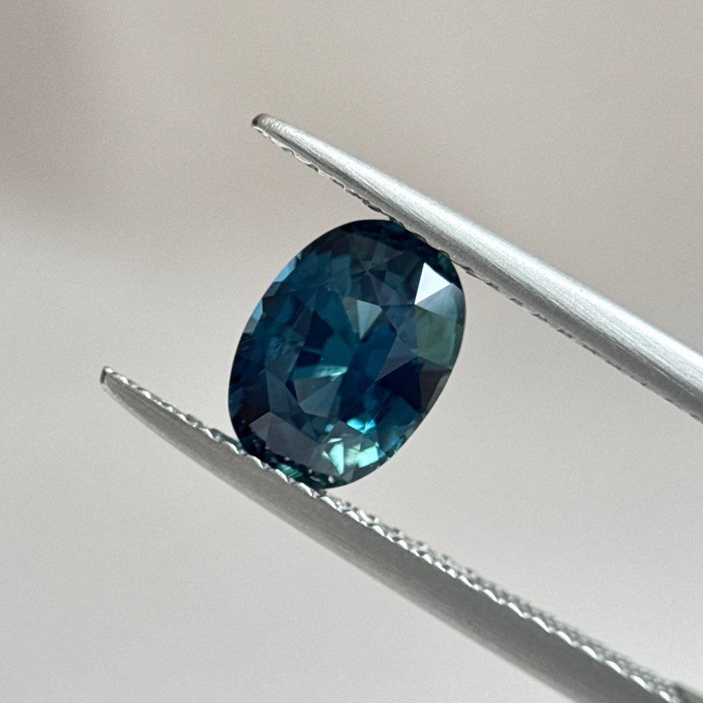 Teal oval sapphire between tweezers by MOHSTEN