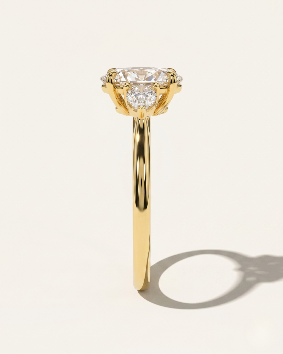 Side profile view of the MOHSTEN Valencia oval and pear diamond trilogy engagement ring in 18ct yellow gold highlighting the fluid band thickness and structural trilogy setting layout.