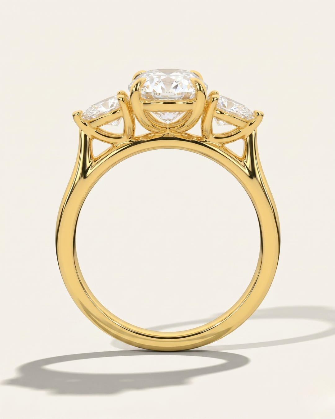 Through-finger architectural view of the MOHSTEN Valencia oval and pear diamond trilogy engagement ring in 18ct yellow gold highlighting the low-profile gallery setting.