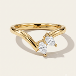 A gold ring with a curved, openwork band and two pear-cut clear gemstones, photographed on a clean off-white background with a soft shadow.