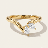 A gold ring with a curved, openwork band and two pear-cut clear gemstones, photographed on a clean off-white background with a soft shadow.